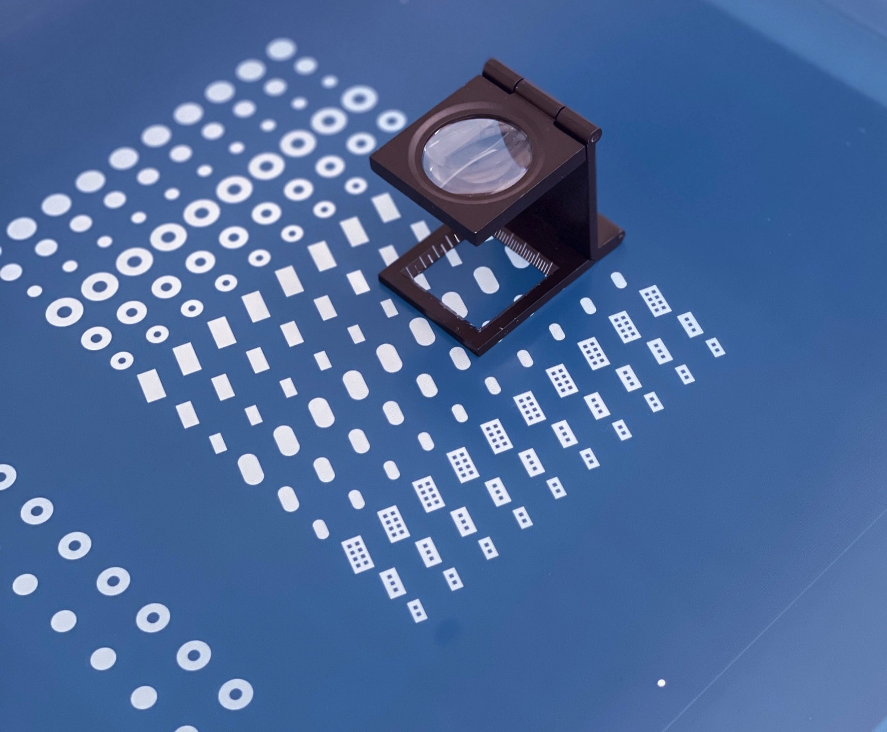 Rows of small 3D screen-printed tablets on a blue plate, with a magnifying loupe